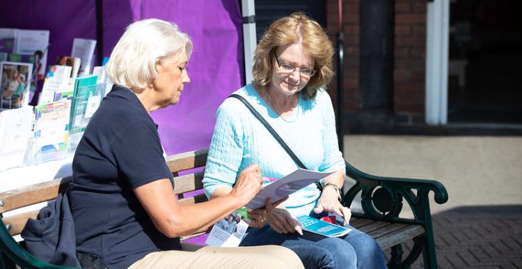 Two women sitting on a bench chatting and looking at paperwork