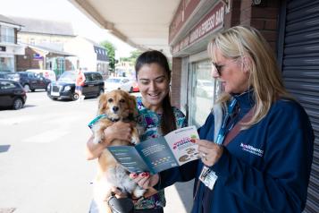 A female Healthwatch staff member is showing a pamphlet to a woman who is holding a dog.