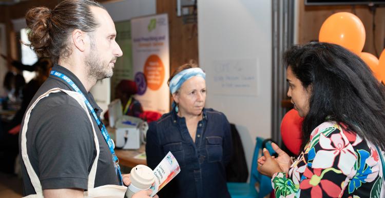 Two women and one man standing in a semi-circle having a conversation in a community hall.