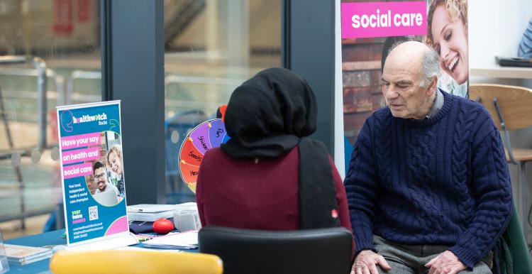two people in conversation in front of a Healthwatch banner display