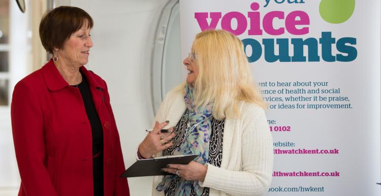 Volunteer speaking to a member of the public in front of a sign Volunteer speaking to a member of the public in front of a sign