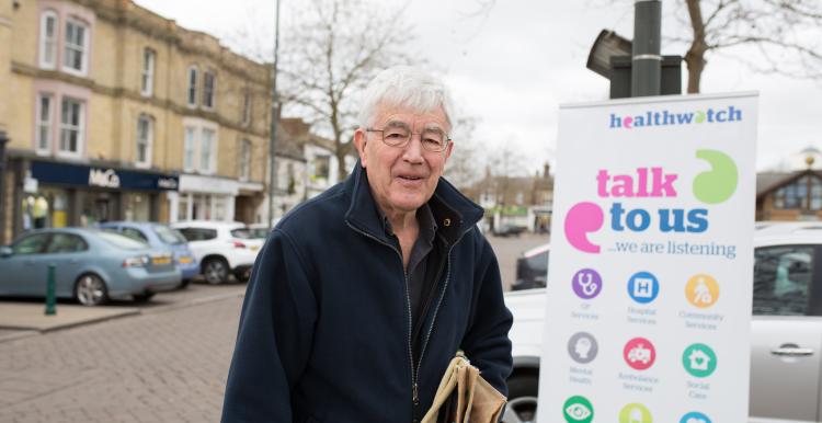 Elderly man standing in front of a Healthwatch banner Elderly man standing in front of a Healthwatch banner