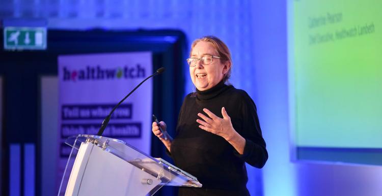 A woman stands in front of a podium, speaking into a microphone at a conference.