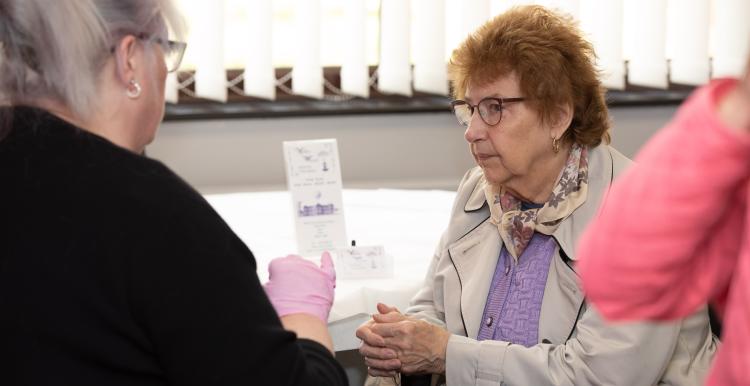 An elderly woman is listening to a therapist speak. The therapist is pointing to a leaflet she is holding