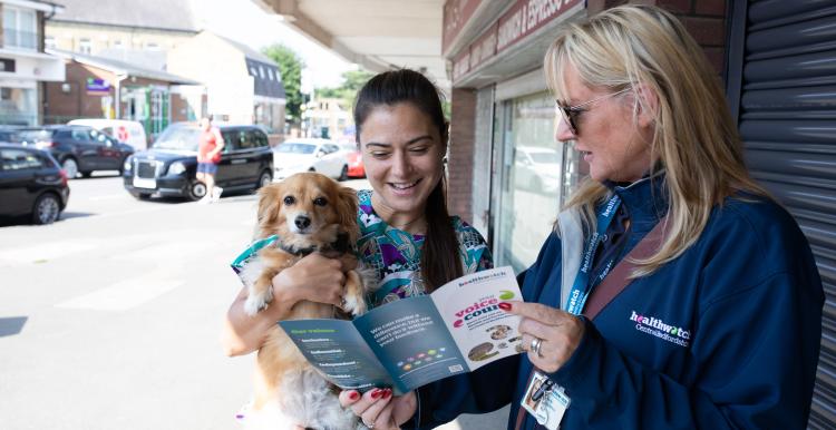 A female Healthwatch staff member is showing a pamphlet to a woman who is holding a dog.