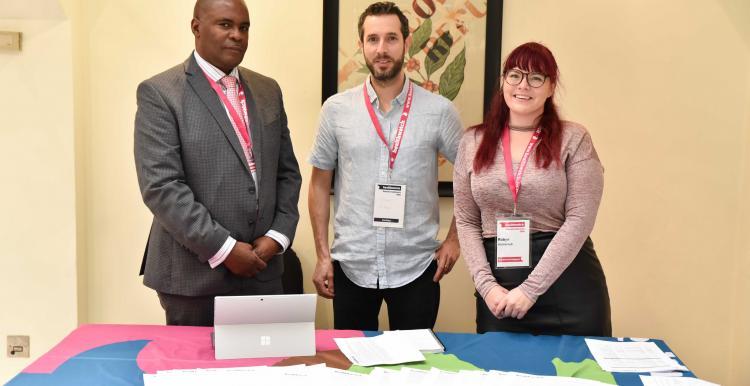Two men and one woman standing together in front of a table Two men and one woman standing together in front of a table