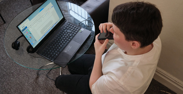 A person sitting at a desk using a laptop computer and a mobile phone