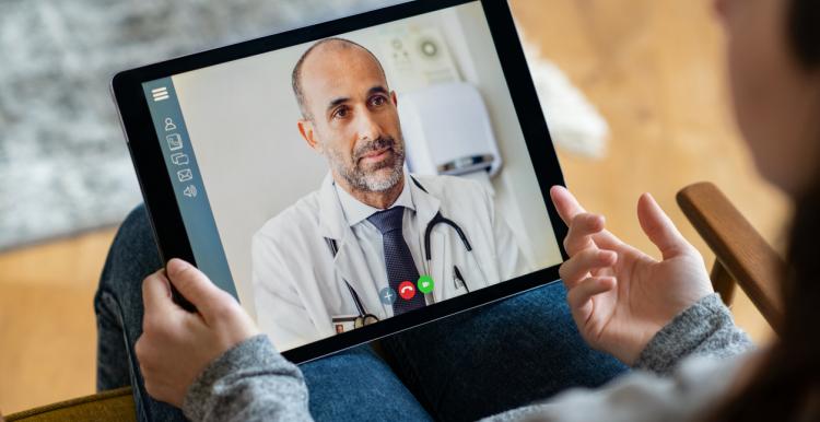 Back view of young woman making video call with her doctor while staying at home.