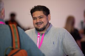 A middle aged man of colour is smiling as he speaks to a colleague in the foreground