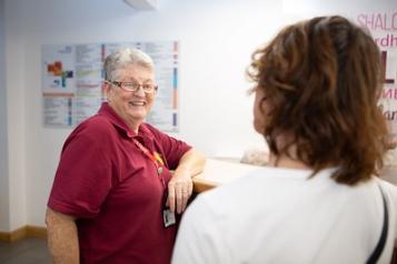 An older female Healthwatch volunteer smiles at a patient in a hospital setting