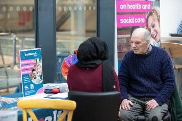 two people in conversation in front of a Healthwatch banner display