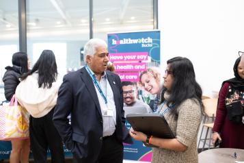 Two people in discussion with Healthwatch banner in background 