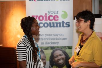 Two women talking in front of a Healthwatch pop up banner