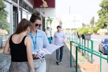 Two women stood outside a building reading a leaflet.  Man walking towards them. 