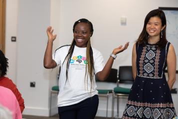 Two women presenting to a group - one with hands in the air.  Both smiling. 