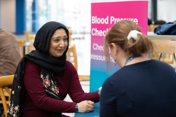 Two women talking across a table next to a blood pressure check pop up banner