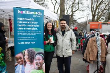 Man and woman standing next to Healthwatch pop up banner in outdoor market
