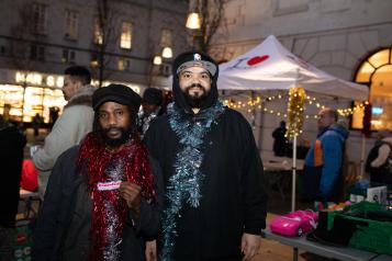 Two men standing next to each other at an outdoor event wearing tinsel around their necks