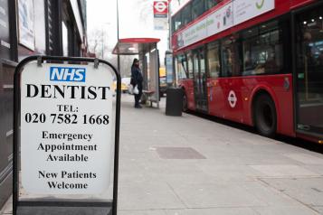 Picture of a sign on a street advertising NHS dentist. Red bus in background. 