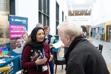 Female volunteer talking to a man in front of a Healthwatch pop up banner at an outdoor event