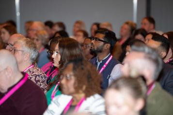 Group of people all sitting in rows of chairs wearing Healthwatch lanyards and facing forwards. 