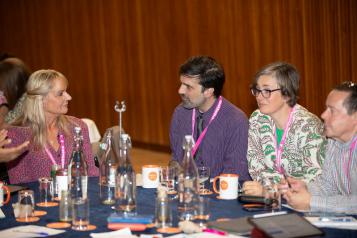 Four people sat at a table talking wearing Healthwatch lanyards