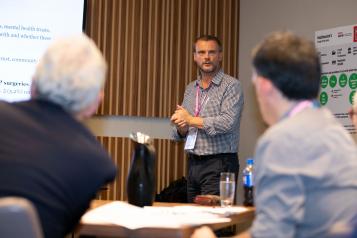 Man stood in front of a room of people giving a talk