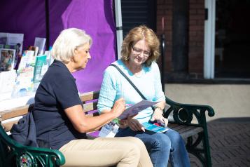 Two women sitting on a bench chatting and looking at paperwork