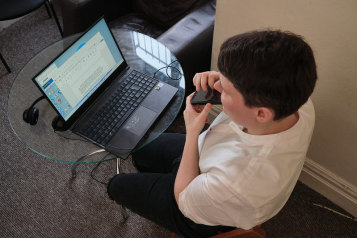 A person sitting at a desk using a laptop and a mobile phone