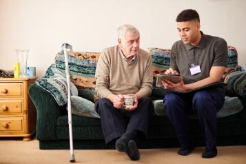 Carer sitting with elderly man on sofa