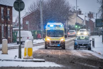 NHS EMAS Ambulance Service on 999 emergency response with snow on road blue lights during snowfall stock photo