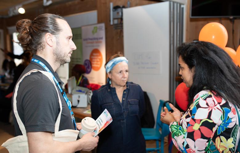 Two women and one man standing in a semi-circle having a conversation in a community hall.