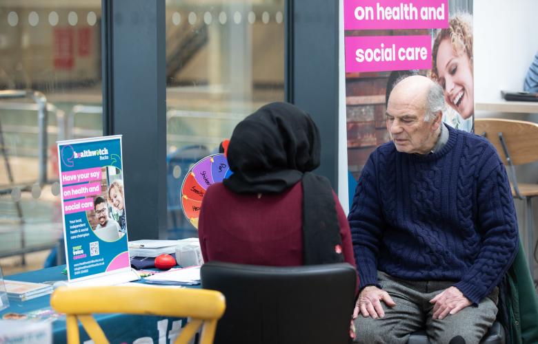 two people in conversation in front of a Healthwatch banner display
