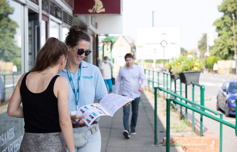 Two women stood outside a building reading a leaflet.  Man walking towards them. 